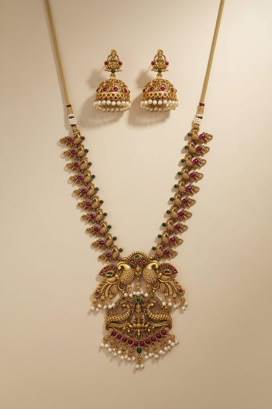Ornate gold necklace with red stones and matching earrings on a beige background
