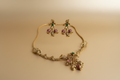 Gold necklace with floral designs and gemstones on a beige background