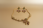 Gold necklace with floral designs and gemstones on a beige background