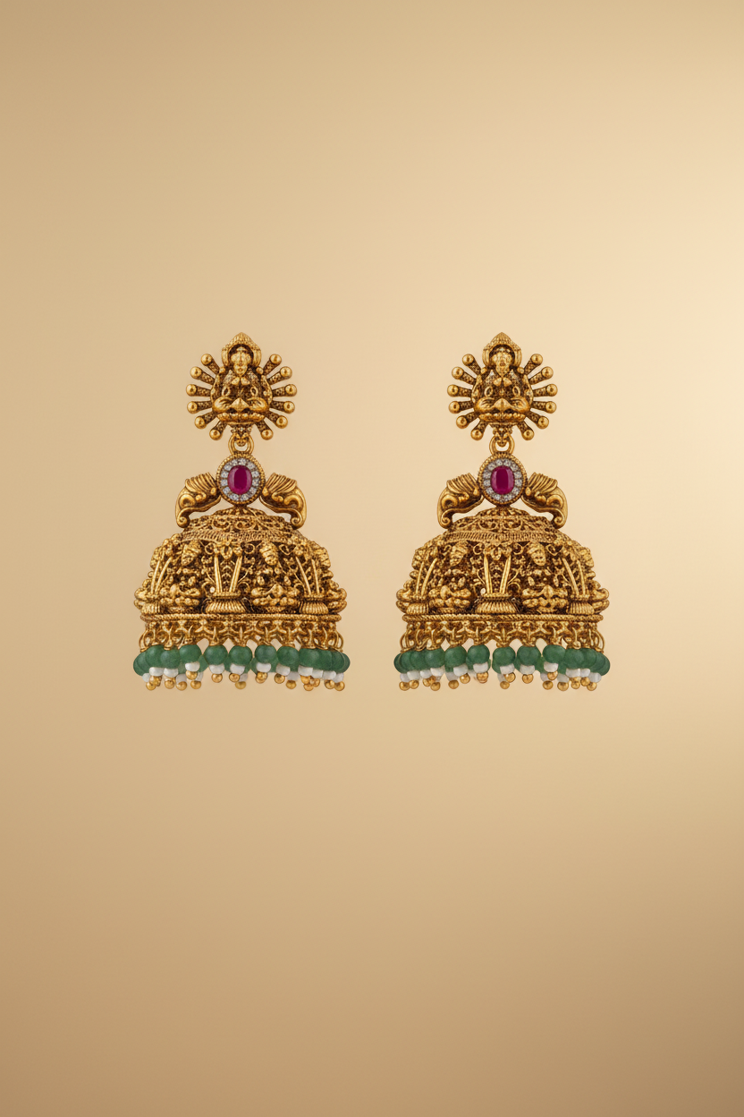 Pair of gold earrings with red and green stones on a beige background