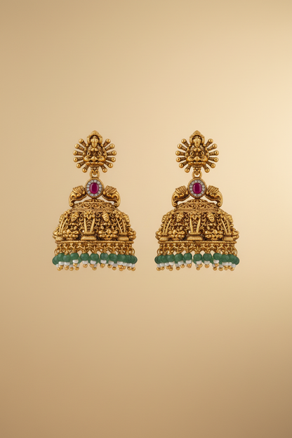 Pair of gold earrings with red and green stones on a beige background