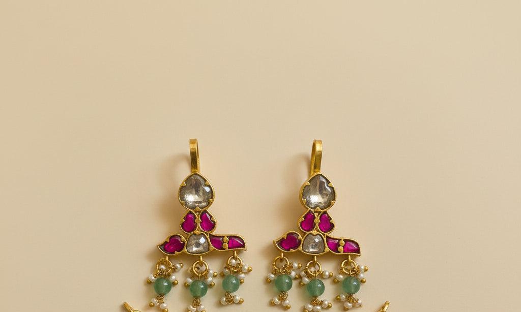 Gold pendant with red and green gemstones on a textured white surface