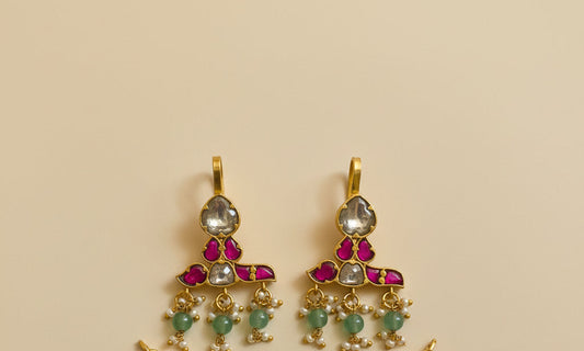 Gold pendant with red and green gemstones on a textured white surface