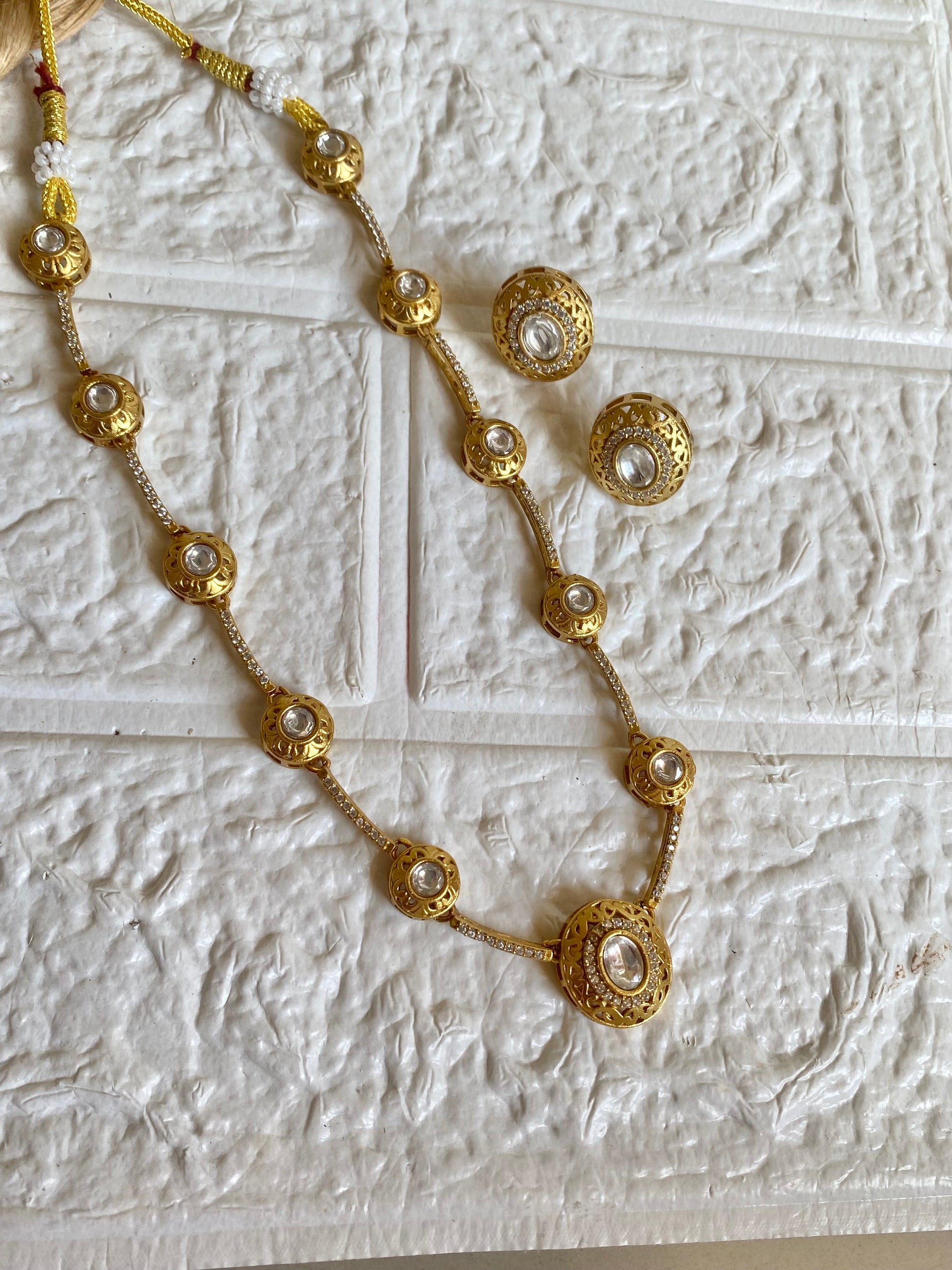 Gold necklace with pearl-like beads on a textured white surface