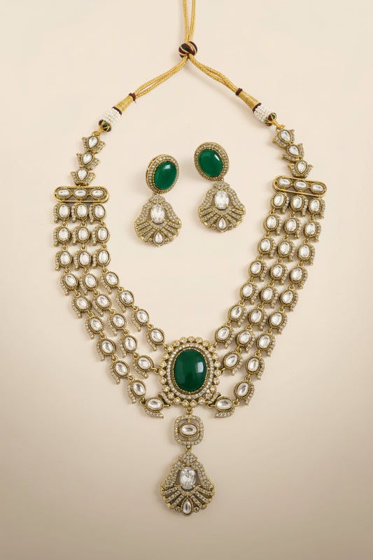Gold necklace with green stones and matching earrings on a textured white surface